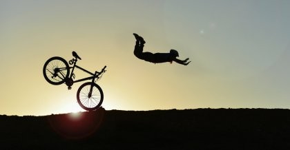 Eine Silhouette im Gegenlicht fliegt wegen zu starker Bremsen über ihr Fahrrad.