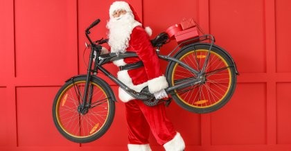 Ein Weihnachtsmann trägt ein Fahrrad als Geschenk.