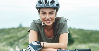 Eine junge Frau mit Fahrradhelm lehnt sich locker auf ihren Lenker und schaut lächelnd in die Kamera.