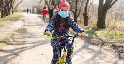 Ein Kind mit Mundschutz fährt auf dem Fahrrad durch den Park