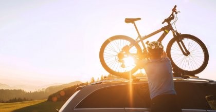 Ein Mann hebt ein Fahrrad im Sonnenuntergang auf ein Autodach.
