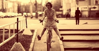 Ein Sepia-Foto zeigt eine Frau im Kleid auf einem Fahrrad.