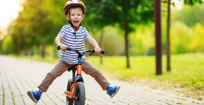 Kleiner Junge fährt mit einem Laufrad durch einen Park